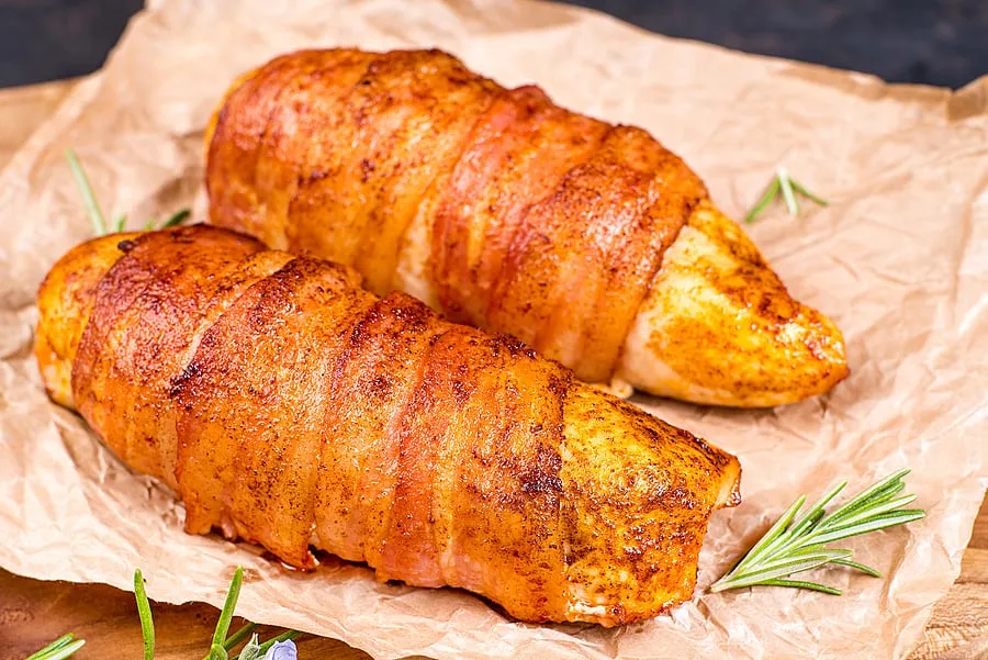 chicken fillet wrapped with bacon slices on a wooden kitchen boa